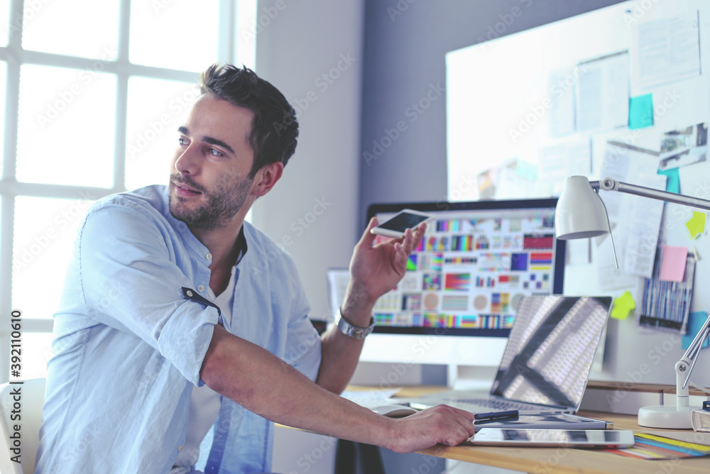 Poster portrait of young designer sitting at graphic studio in front of laptop and computer while working o