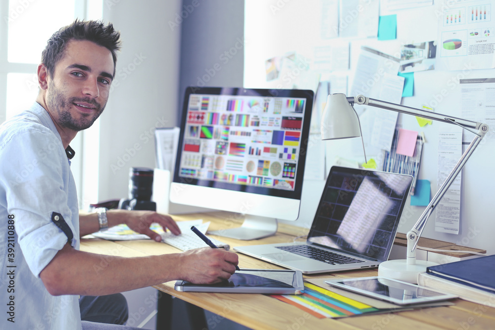 Poster portrait of young designer sitting at graphic studio in front of laptop and computer while working o