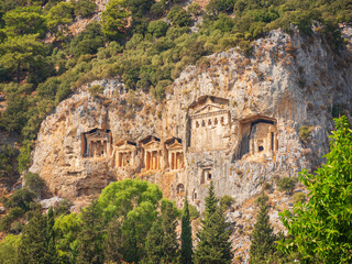 Fototapeta na wymiar view to antique tombs in rock above green forest in Turkey