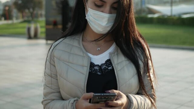 brunette Girl in mask in outdoor look to the mobile phone and wear the mask