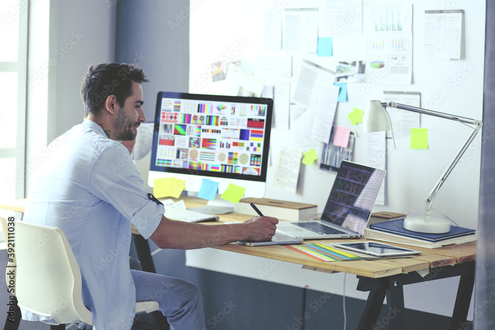 Poster portrait of young designer sitting at graphic studio in front of laptop and computer while working o
