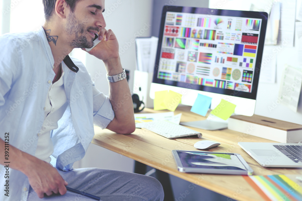 Poster portrait of young designer sitting at graphic studio in front of laptop and computer while working o