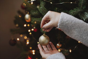 Decorating christmas tree with modern golden bauble in festive decorated room with lights
