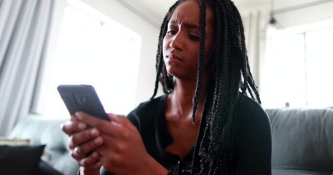 Upset African teen girl reacting to negative text message on smartphone device