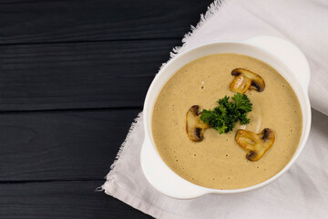 Puree soup with mushrooms and herbs, in a white plate, on a wooden background. View from above