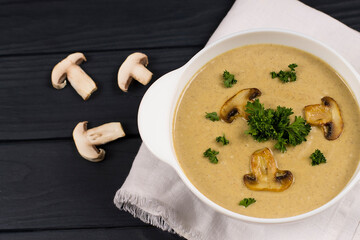 Puree soup with mushrooms and herbs, in a white plate, on a wooden background. View from above