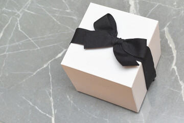 Gift wrapped present box with a black bow on marble background