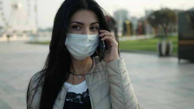 brunette Girl in mask in outdoor look to the mobile phone and wear the mask