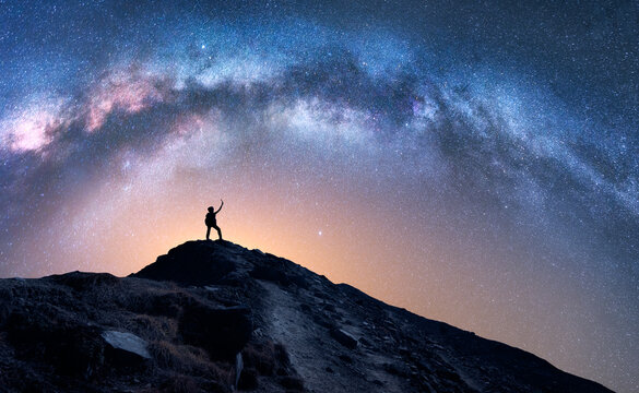 Arched Milky Way And Happy Man On The Mountain At Night. Silhouette Of Guy With Raised Up Arm On The Hill, Sky With Stars, Yellow Light In Nepal. Galaxy. Space Landscape With Milky Way Arch. Travel