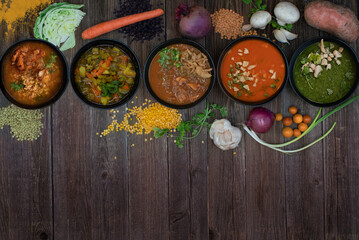 An assortment of vegan soup bowls with scattered ingredients on wooden table, copy space