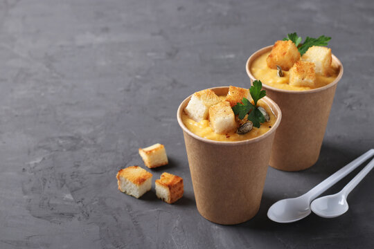 Thick vegan pumpkin cream soup with seeds and croutons in disposable cups of craft paper. Soup to go. Healthy food delivery. Take away food.
