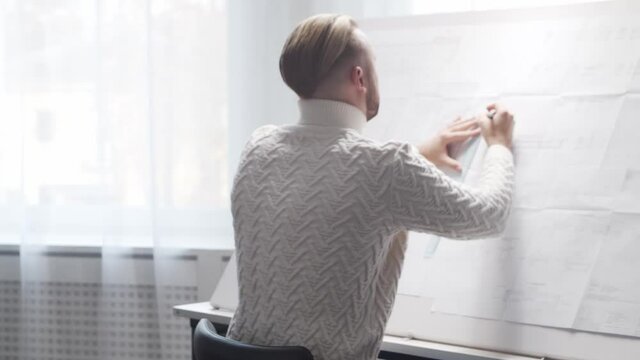 Concentrated architect works in loft using drawing board. Workplace of young engineer in modern office.