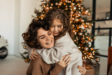 Charming lovable caucasian woman with curves hugging with her little daughter and celebrating Christmas and New Year