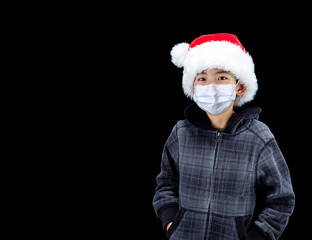 Fototapeta na wymiar Boy Wearing Santa Hat and Face Mask During Covid-19 Christmas Pandemic With Copy Space