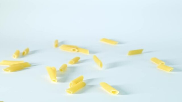 Raw uncooked renne pasta falling down in super slow motion against white background, slow mo