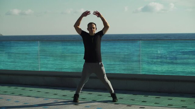 A young guy does morning exercises on a sunny day. A young man goes in for sports outdoors on the background of the sea. 4k