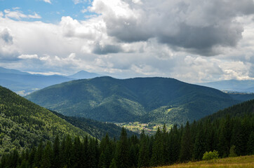 Fototapeta na wymiar Landscape with forest, mountains and small Carpathian village in the valley under cloudy sky 