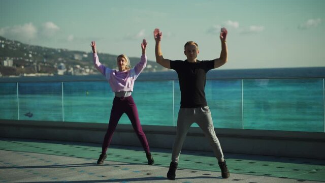 Young couple in sportswear are engaged in morning exercises against the background of the sea. The guy and the girl go in for sports together. 4k