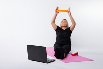 Online senior woman workout with elastic band sitting on fitness mat. Online training over the Internet at home. Pandemic. Photo on white background
