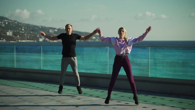Young couple in sportswear are engaged in morning exercises against the background of the sea. The guy and the girl go in for sports together. 4k