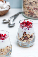 Homemade yougurt with granola and pomegranate fruit in glasses on white wooden table. Healthy breakfast.