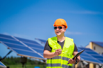 Engineer in sun glasses and helmet on a background of solar energy power station. Clipboard in hands.