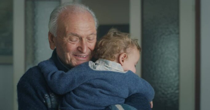 Cinematic shot of tender senior gray hair grandfather is cuddling a grandson baby while sleeping peacefully on  his arms at home.Concept of life, grandparents, love, care, generation, childhood