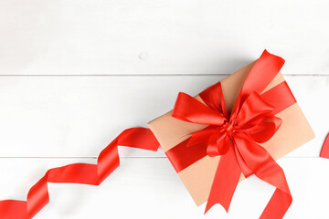 Gift box wrapped in craft recycled paper with red ribbon bow on a white wooden backgroud. Christmas or San Valentino present, top view, copy space