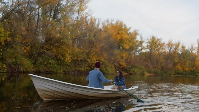 A handsome guy and a beautiful girl swim in a boat on a lake in a fairy autumn forest