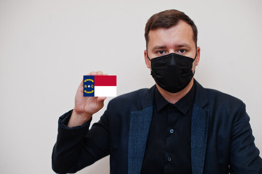 Man wear black formal and protect face mask, hold Alabama flag card isolated on white background. USA coronavirus Covid country concept.