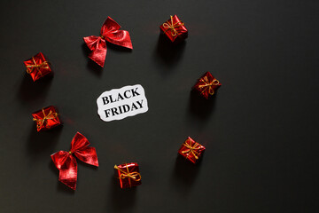 Black Friday holiday shopping concept. Advertising message on a paper sheet and red gifts on a black background.	