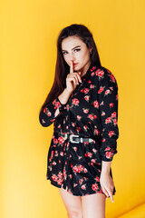 Beautiful fashionable brunette woman in a dress with flowers finger at the lips