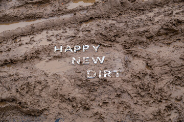 the words happy new dirt laid with silver metal letters on wet mud surface