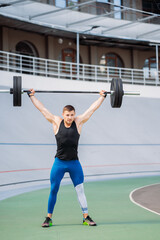 Young guy raises the bar in the stadium, outdoor workout