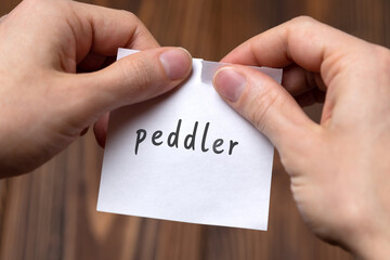 Hands of a man tearing a piece of paper with inscription peddler