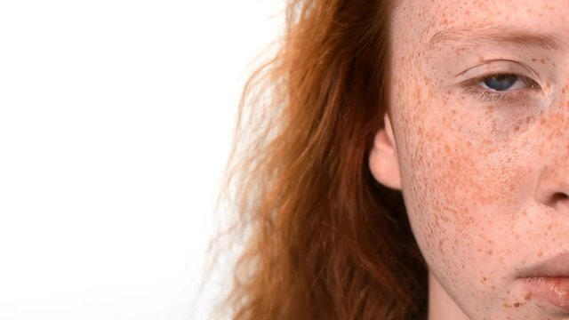 Red haired girl with lots of freckles on the face and blue eyes looking into the camera. White background. Close up