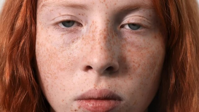 Red haired girl with lots of freckles on the face and blue eyes looking into the camera. White background. Close up