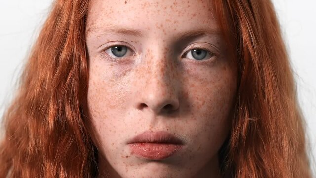 Red haired girl with lots of freckles on the face and blue eyes looking into the camera. White background. Close up