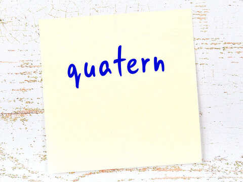 Yellow sticky note on wooden wall with handwritten word quatern