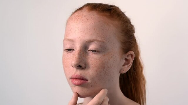 Red haired girl with lots of freckles on the face and blue eyes looking into the camera. White background. Close up