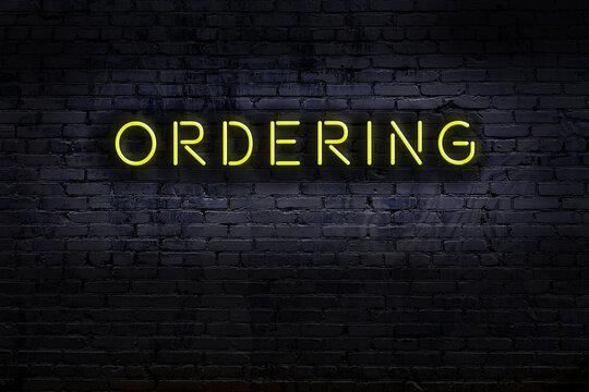 Neon sign. Word ordering against brick wall. Night view