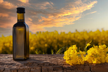 Rapeseed oil in bottles on white wooden table on background flowering rape field.