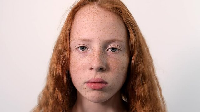 Red haired girl with lots of freckles on the face and blue eyes looking into the camera. White background. Close up