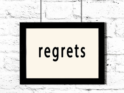 Black frame hanging on white brick wall with inscription regrets