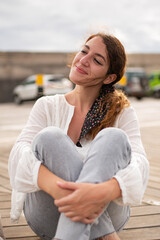 Smiling young woman sitting on a wooden walkway.