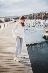 Young woman standing, dressed in blouse and jeans, looking at the water in a sea port.