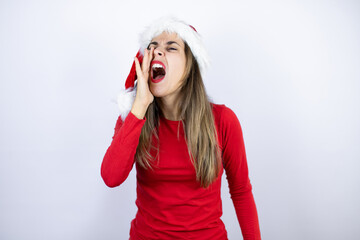 Young beautiful woman wearing a Santa hat over white background shouting and screaming loud to side with hand on mouth