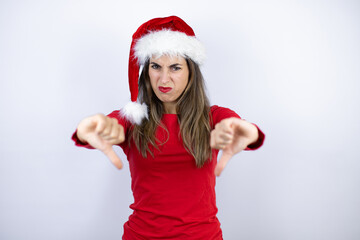 Young beautiful woman wearing a Santa hat over white background with angry face, negative sign showing dislike with thumbs down