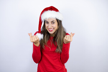 Young beautiful woman wearing a Santa hat over white background doing money gesture with hands, asking for salary payment, millionaire business