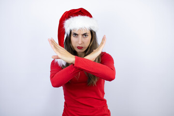 Young beautiful woman wearing a Santa hat over white background Rejection expression crossing arms doing negative sign, angry face